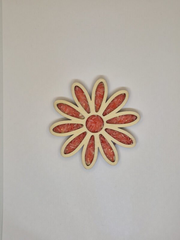 Sensorische vulvorm bloem– rode speelrijst Houten sensorische vulvorm in de vorm van een bloem gevuld met rode speelrijst, geschikt voor sensorisch spel en fijne motoriek.