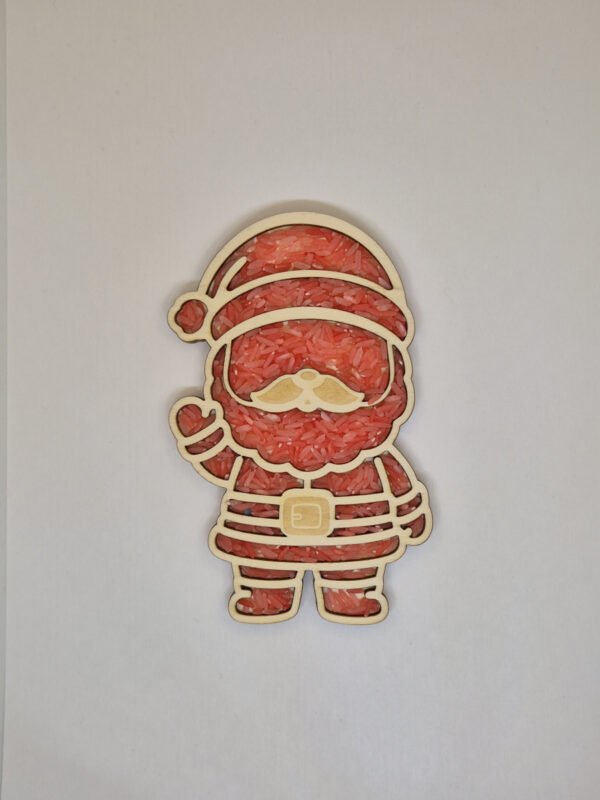 Sensorische vulvorm kerstman– rode speelrijst Houten sensorische vulvorm in de vorm van een kerstman gevuld met rode speelrijst, geschikt voor sensorisch spel en fijne motoriek.