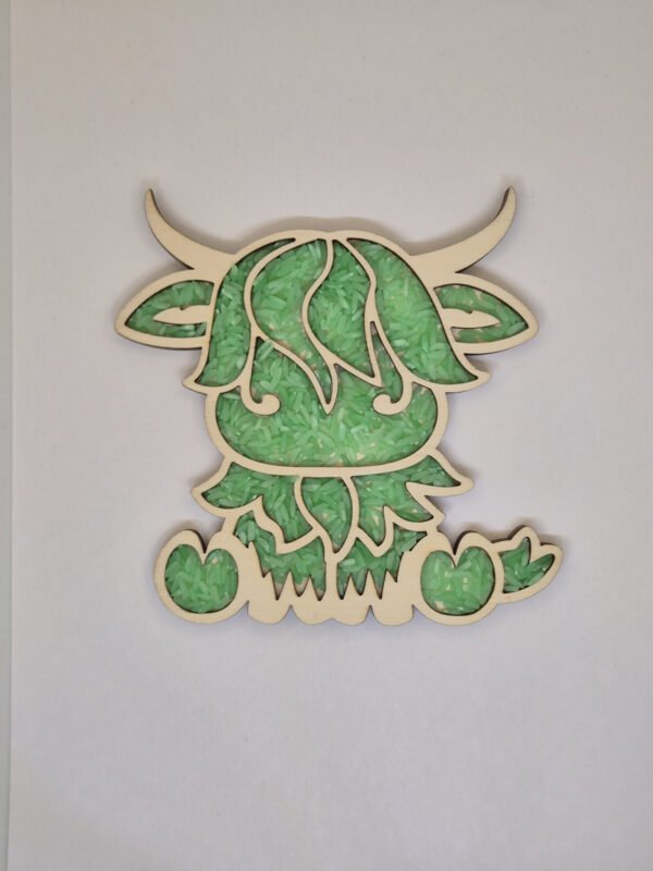 Sensorische vulvorm schotse hooglander– groene speelrijst Houten sensorische vulvorm in de vorm van een schotse hooglander gevuld met groene speelrijst, geschikt voor sensorisch spel en fijne motoriek.