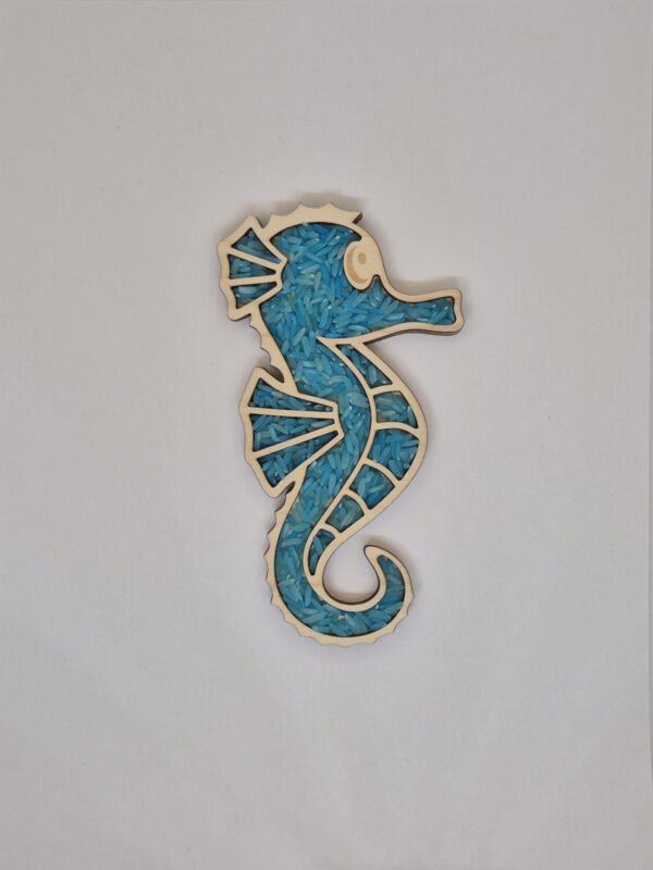 Sensorische vulvorm zeepaardje– blauwe speelrijst Houten sensorische vulvorm in de vorm van een zeepaardje gevuld met blauwe speelrijst, geschikt voor sensorisch spel en fijne motoriek.